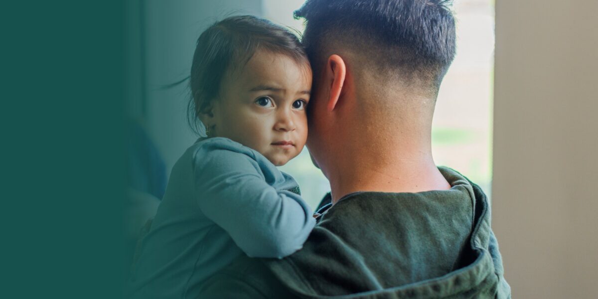 A young child rests her head on her father's shoulder.